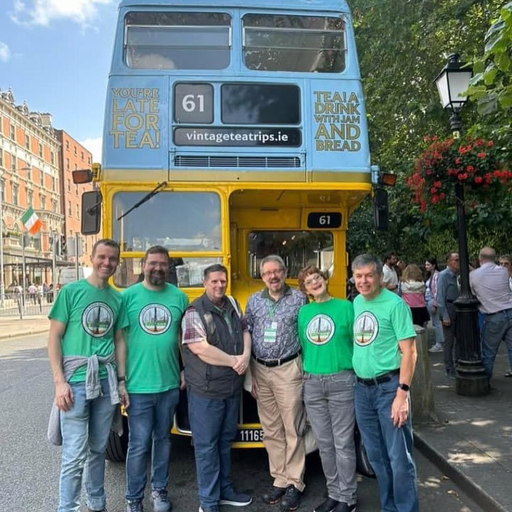 Six choir members in front of a vintage blue and yellow Dublin double-decker bus