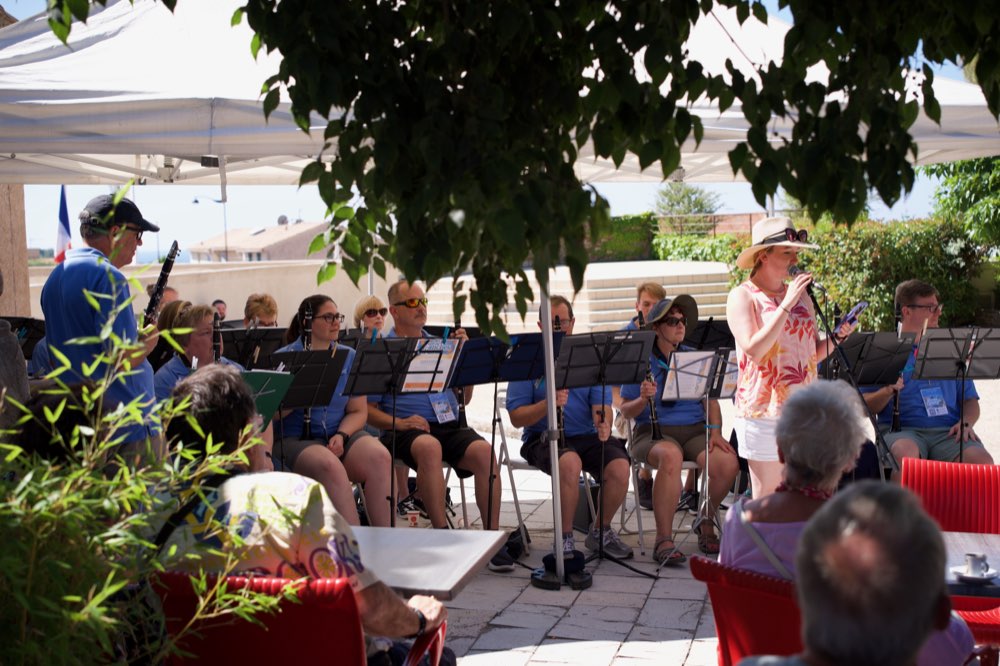 A woman with a microphone introducing the seated Clarinet Choir, café tables in the foreground
