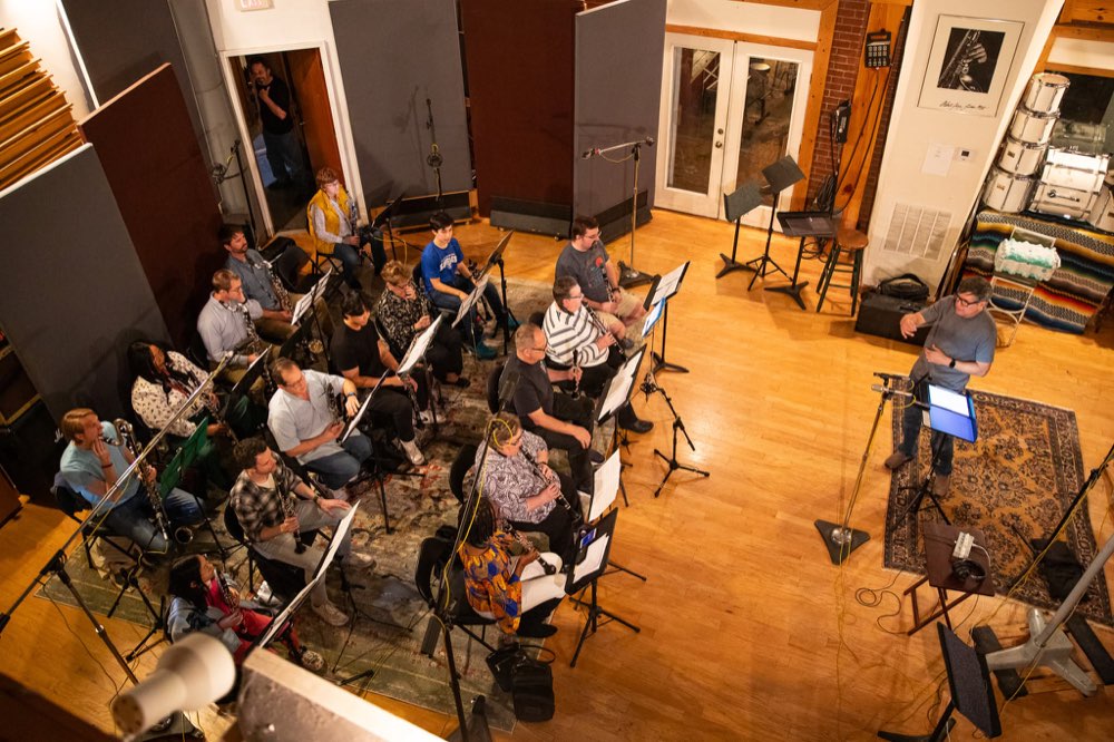 The Clarinet Choir seated in a recording studio, seen from above, with the producer at a mic stand