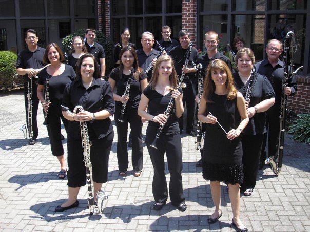 The choir's first members standing outdoors on a brick plaza with their clarinets, one at the front holding a baton