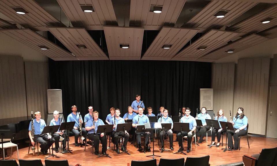 The Clarinet Choir seated with their instruments on a recital hall stage, facing the camera